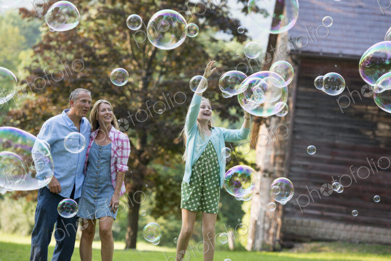 A family sitting on the grass outside a bar, blowing bubbles and laughing.