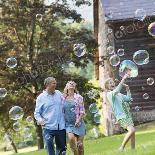 A family sitting on the grass outside a bar, blowing bubbles and laughing.