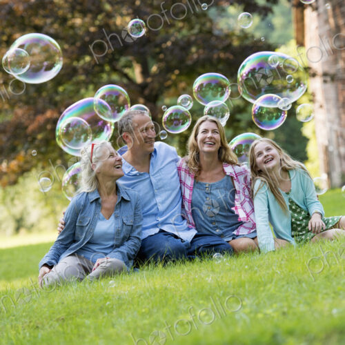 A family sitting on the grass outside a bar, blowing bubbles and laughing.