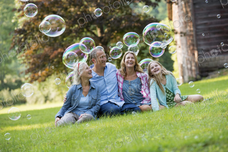 A family sitting on the grass outside a bar, blowing bubbles and laughing.