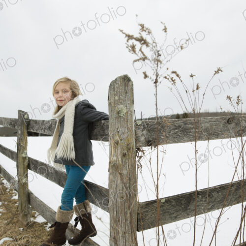 A farm in the snow. A girl with a hat and scarf and boots, leaning on a fence. A farm in the snow. A girl with a hat and scarf and boots, leaning on a fence.