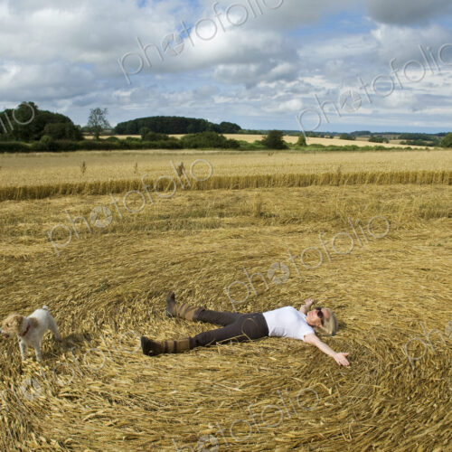 A farmer lying down on his back in the stubble of a freshly cut crop field with arms…