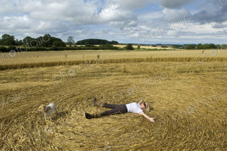 A farmer lying down on his back in the stubble of a freshly cut crop field with arms…