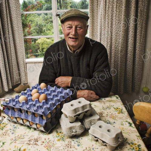 A farmer seated at a table in a farmhouse with trays of fresh eggs. A farmer seated at a table in a farmhouse with trays of fresh eggs.