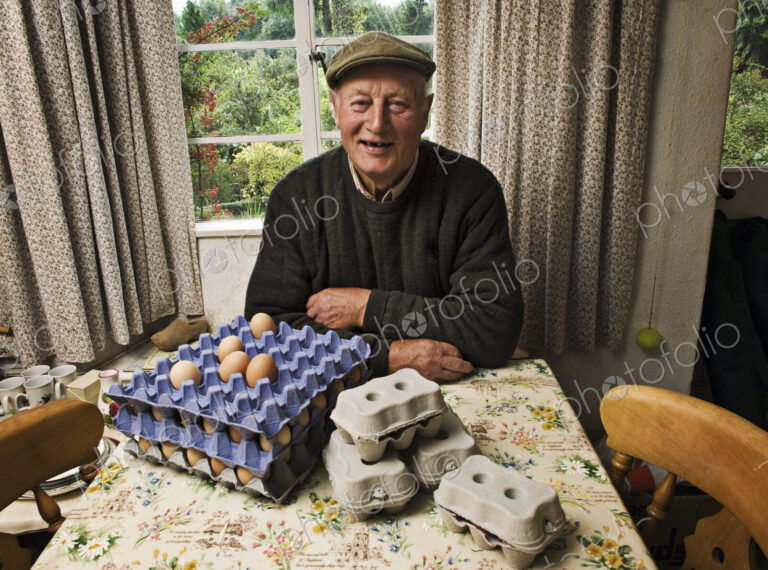 A farmer seated at a table in a farmhouse with trays of fresh eggs.