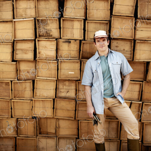 A farmer standing in front of a wall of stacked wooden crates for produce. A farmer standing in front of a wall of stacked wooden crates for produce.