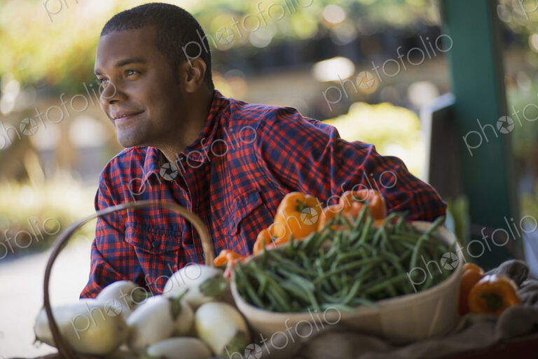 A farmer with a tray of organic bell peppers, green beans and eggplant freshly…