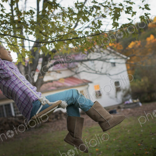 A farmhouse garden, Autumn trees lit by late sunshine. A child seated on a swing. A farmhouse garden, Autumn trees lit by late sunshine. A child seated on a swing.