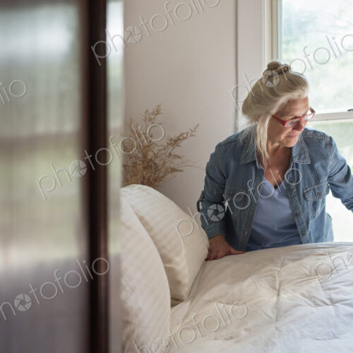 A farmhouse in the country, A woman making up a bed in a bedroom.