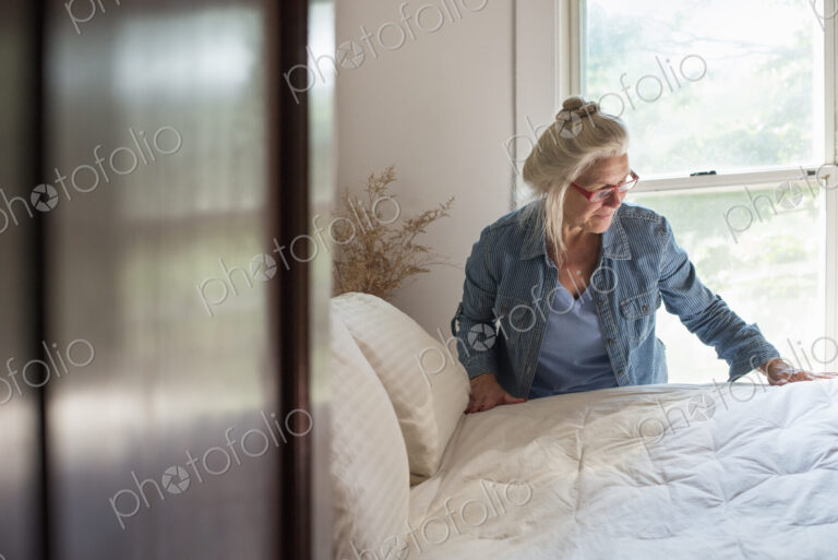 A farmhouse in the country, A woman making up a bed in a bedroom.