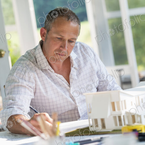 A farmhouse kitchen. A model of a house on the table. Designing a house. A man using a… A farmhouse kitchen. A model of a house on the table. Designing a house. A man using a…