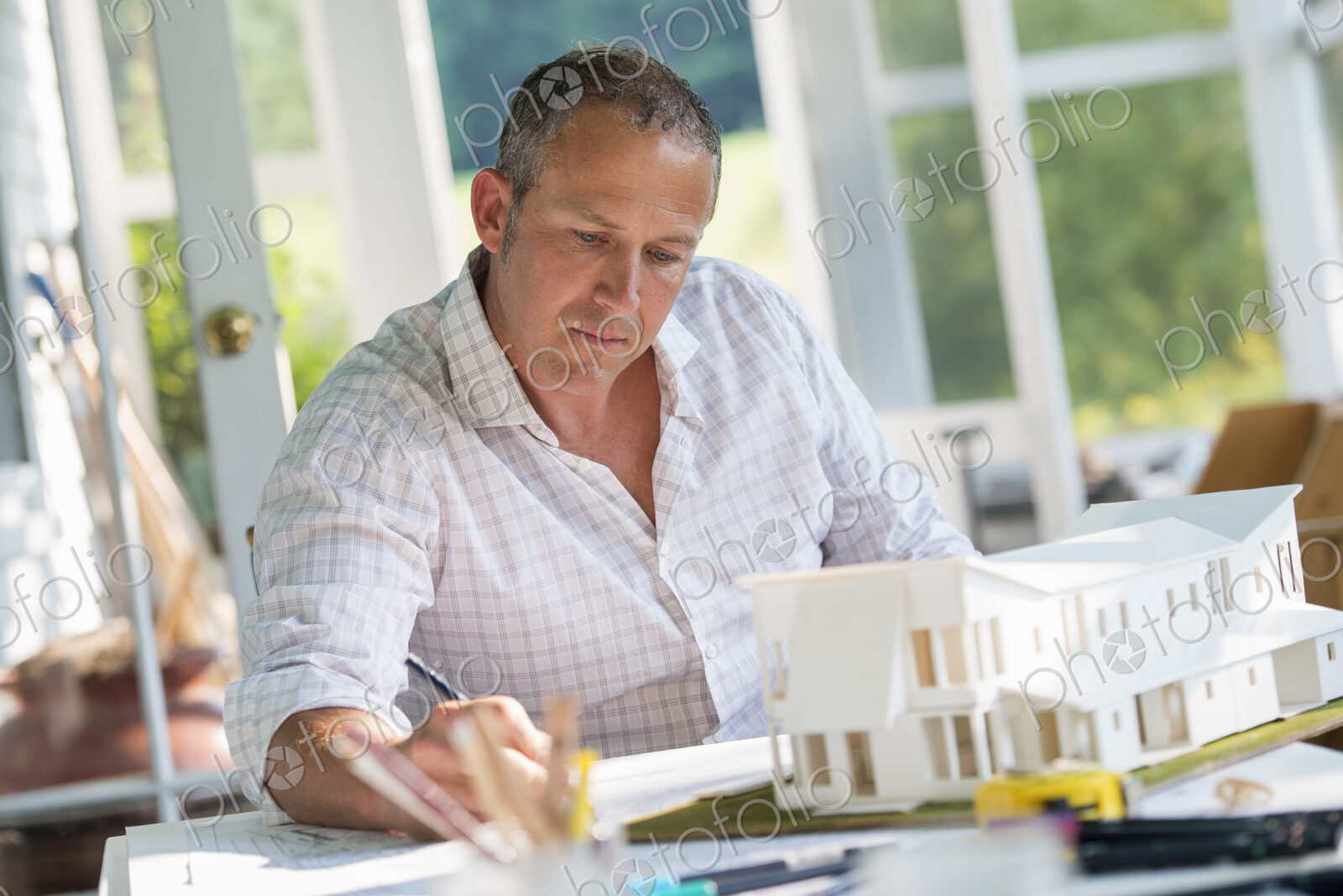 A farmhouse kitchen. A model of a house on the table. Designing a house. A man using a…