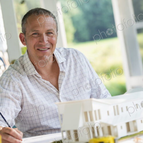 A farmhouse kitchen. A model of a house on the table. Designing a house. A man using a… A farmhouse kitchen. A model of a house on the table. Designing a house. A man using a…