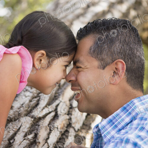 A father and daughter with foreheads pressed together by a tree in the park. A father and daughter with foreheads pressed together by a tree in the park.