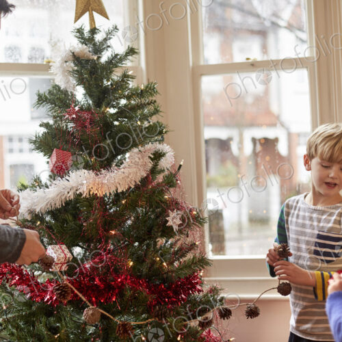 A father and two children decorating a Christmas tree at home.