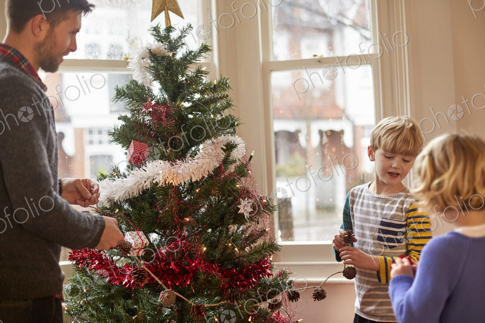 A father and two children decorating a Christmas tree at home.