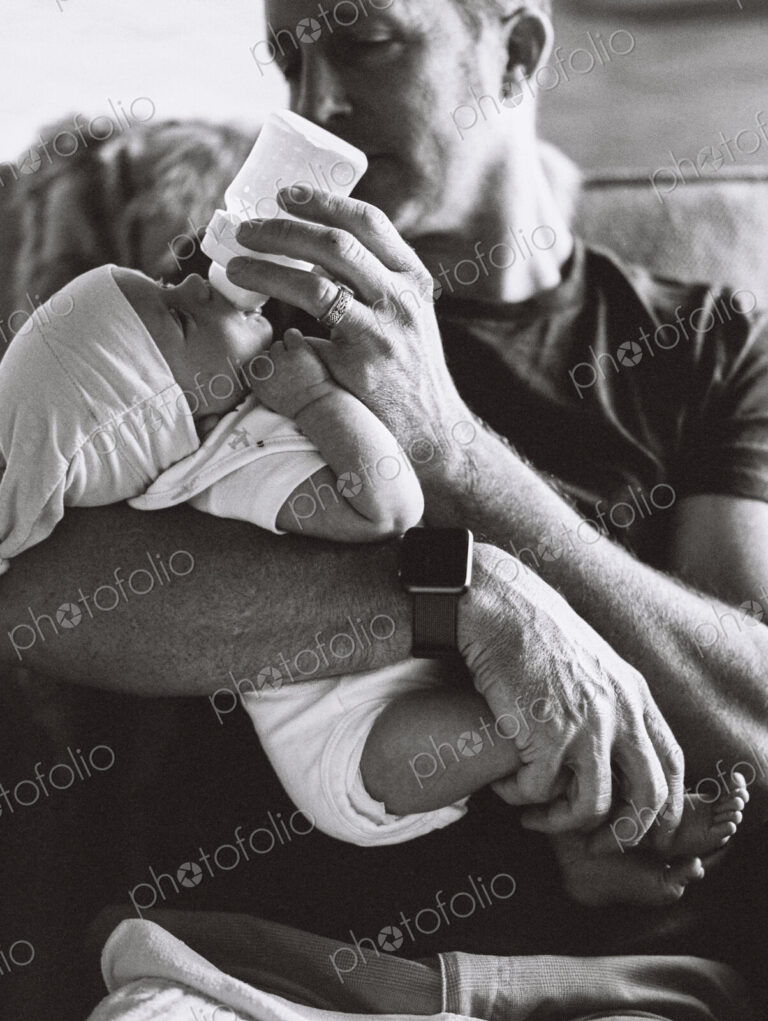 A father cradling a small baby and bottle feeding him.
