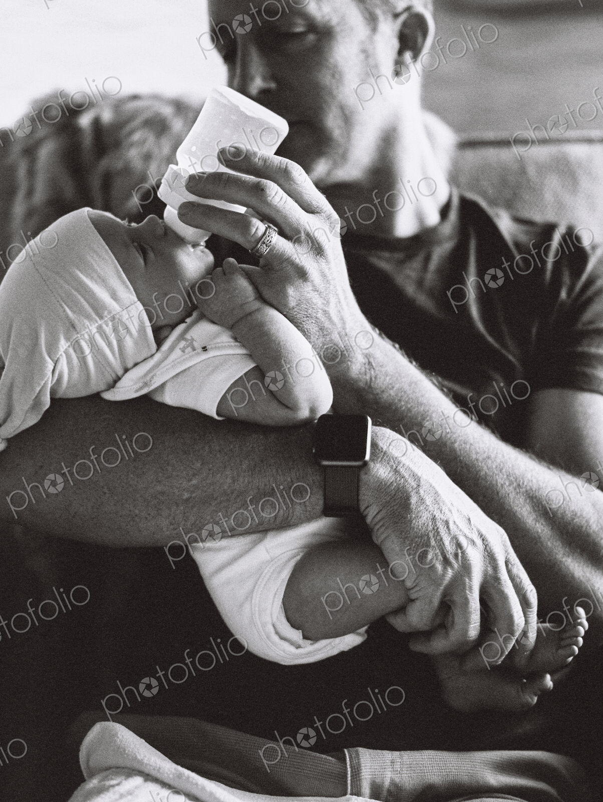A father cradling a small baby and bottle feeding him.
