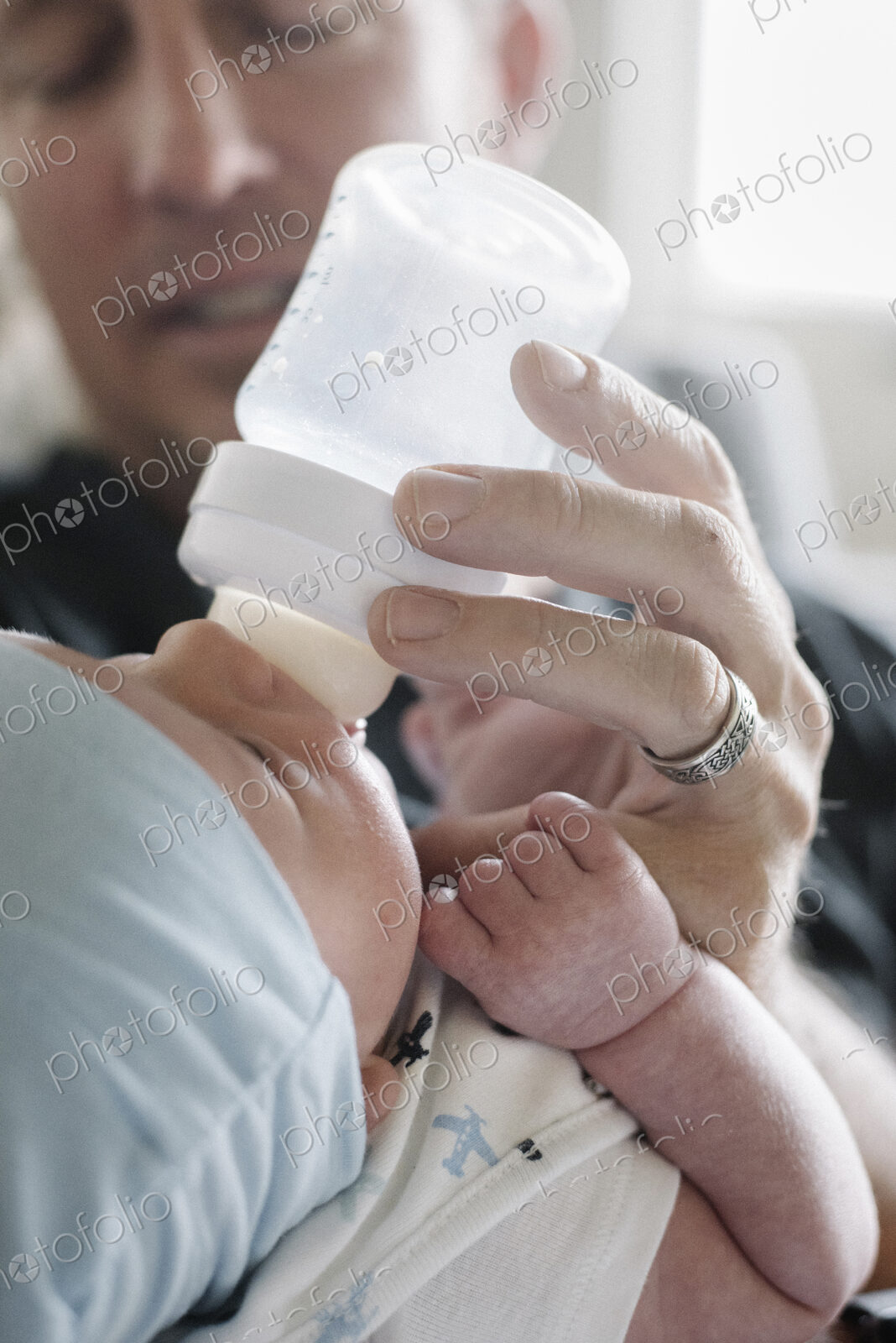 A father cradling a small baby and bottle feeding him.