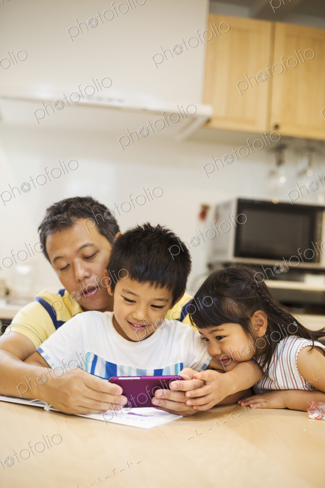 A father, son and daughter sitting at a table playing with a smart phone, looking at…