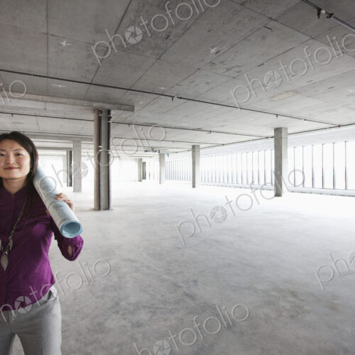 A female Asian architect with a scroll of plans on her shoulder, in a new raw business…