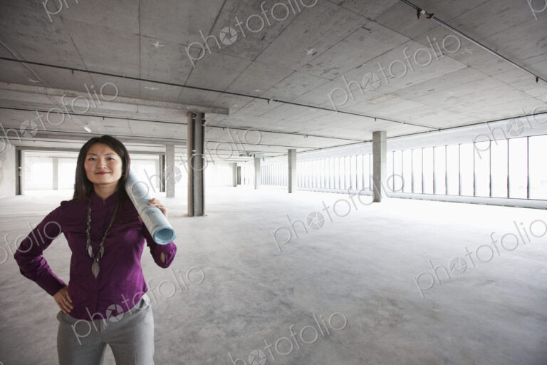 A female Asian architect with a scroll of plans on her shoulder, in a new raw business…