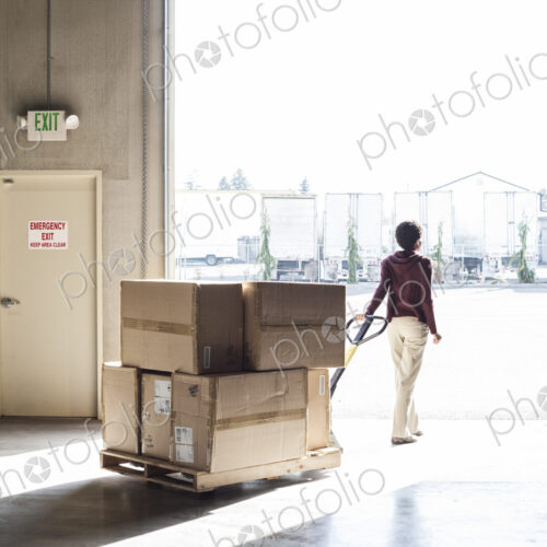 A female warehouse worker moving products with a pallet jack, to a loading door A female warehouse worker moving products with a pallet jack, to a loading door