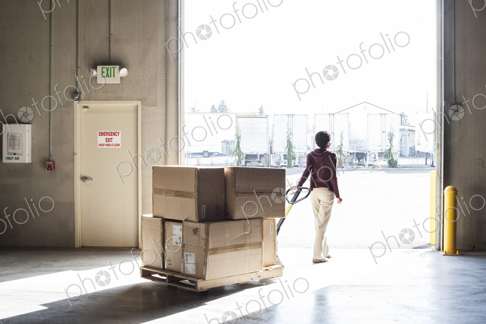 A female warehouse worker moving products with a pallet jack, to a loading door