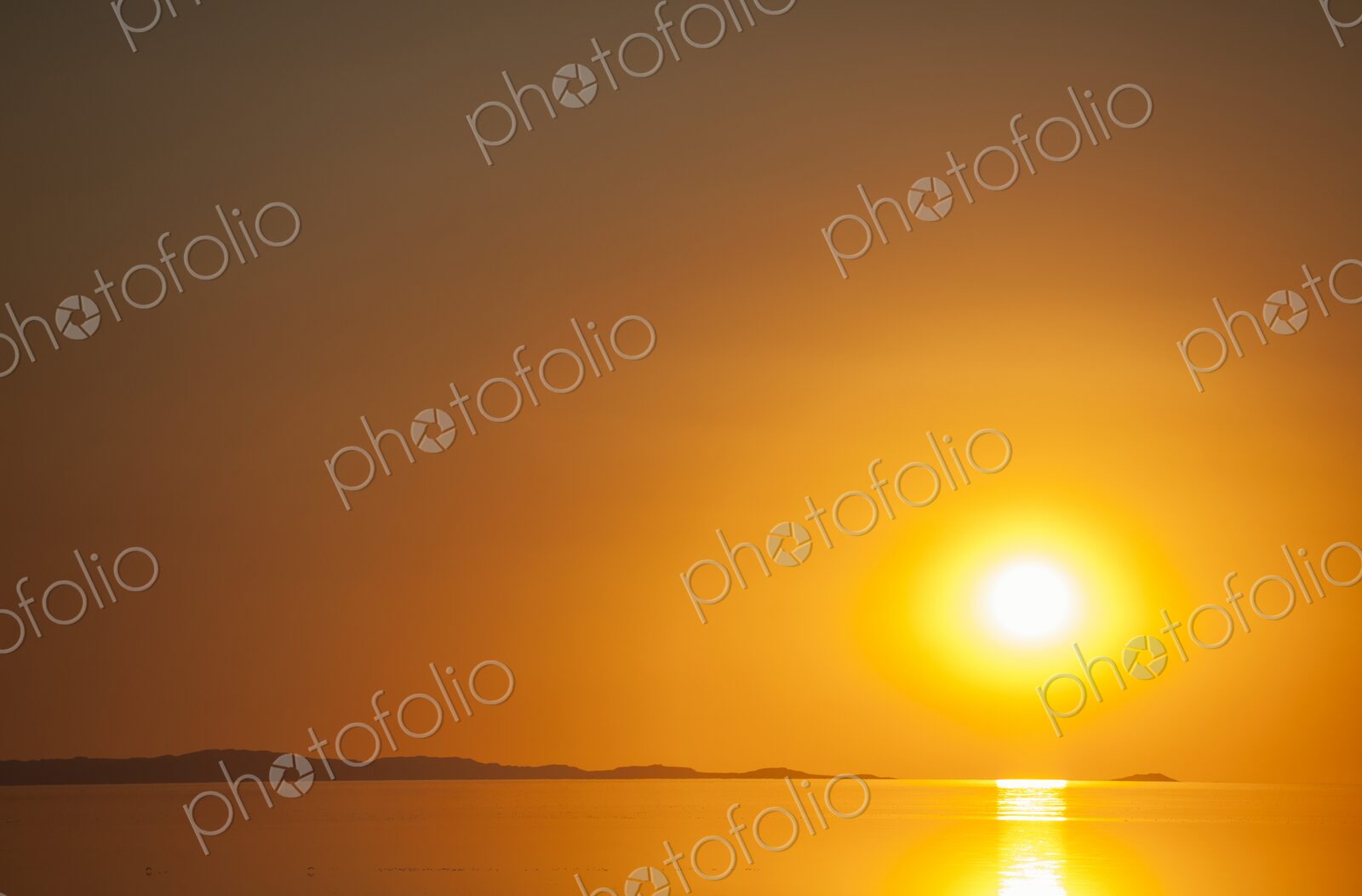 A fiery orange sun sets over the calm surface of the Great Salt Lake, casting golden…