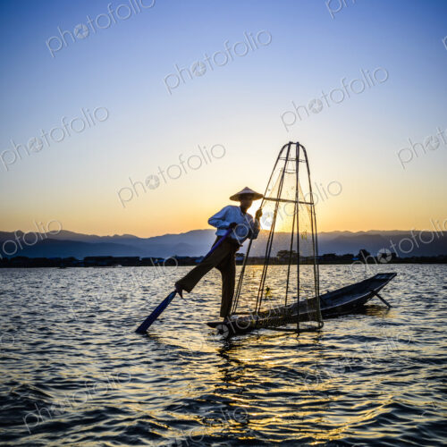 A fisherman on his boat on Lake Inle standing using his leg to move the oar.