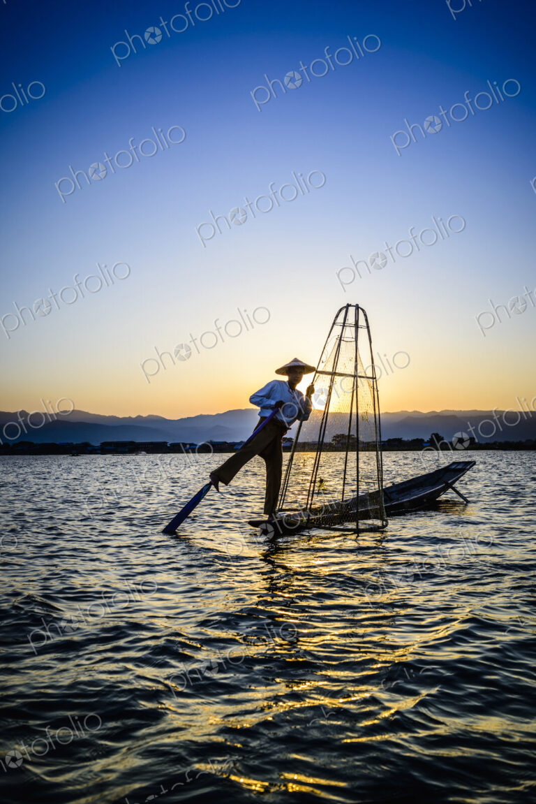 A fisherman on his boat on Lake Inle standing using his leg to move the oar.