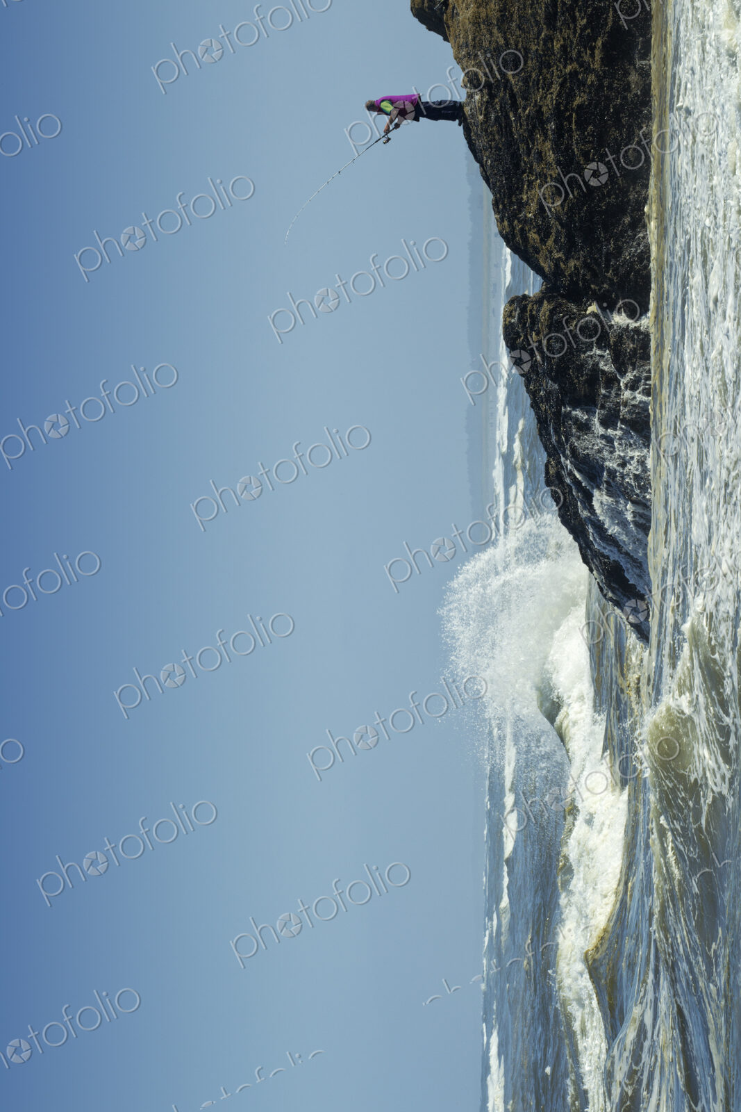 A fisherman on the rocky shore, fishing, waves breaking on shore.