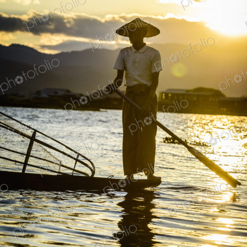 A fisherman standing on his boat fishing on Lake Inle at dusk.