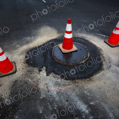 A flood of water from a sewer manhole cover and traffic cones on a road.