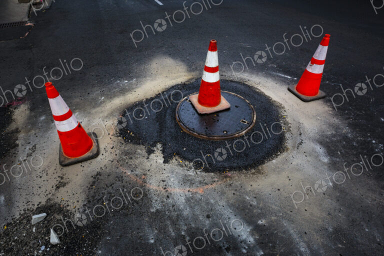 A flood of water from a sewer manhole cover and traffic cones on a road.