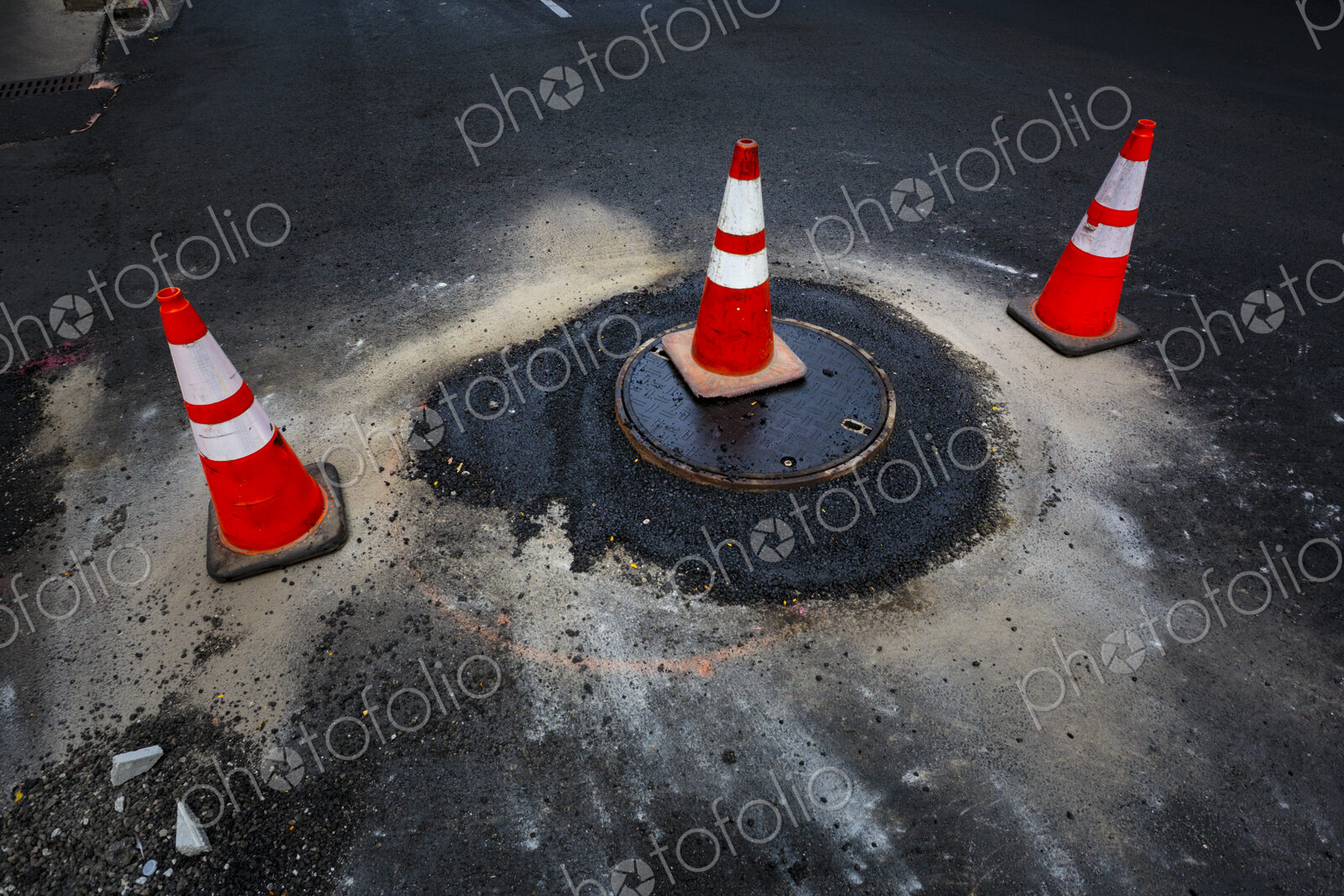 A flood of water from a sewer manhole cover and traffic cones on a road.