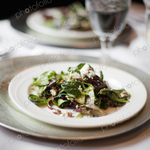 A formal table setting for a meal. China plates and glasses. An organic salad with…