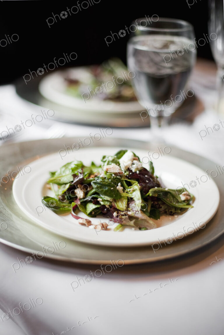 A formal table setting for a meal. China plates and glasses. An organic salad with…