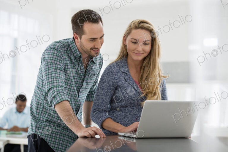 A fresh white building interior, flooded with light. A couple at a table looking at a…