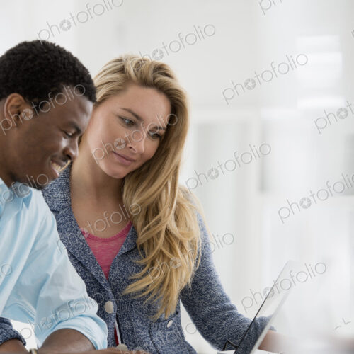 A fresh white building interior, flooded with light. A couple at a table using a laptop. A fresh white building interior, flooded with light. A couple at a table using a laptop.