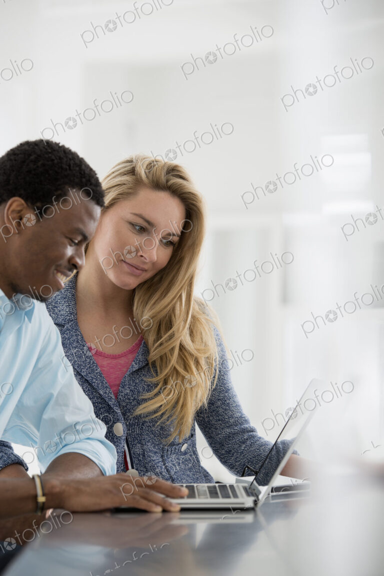 A fresh white building interior, flooded with light. A couple at a table using a laptop.