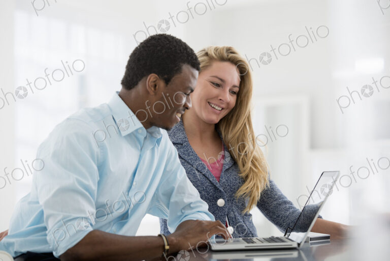 A fresh white building interior, flooded with light. A couple seated side by side at a…