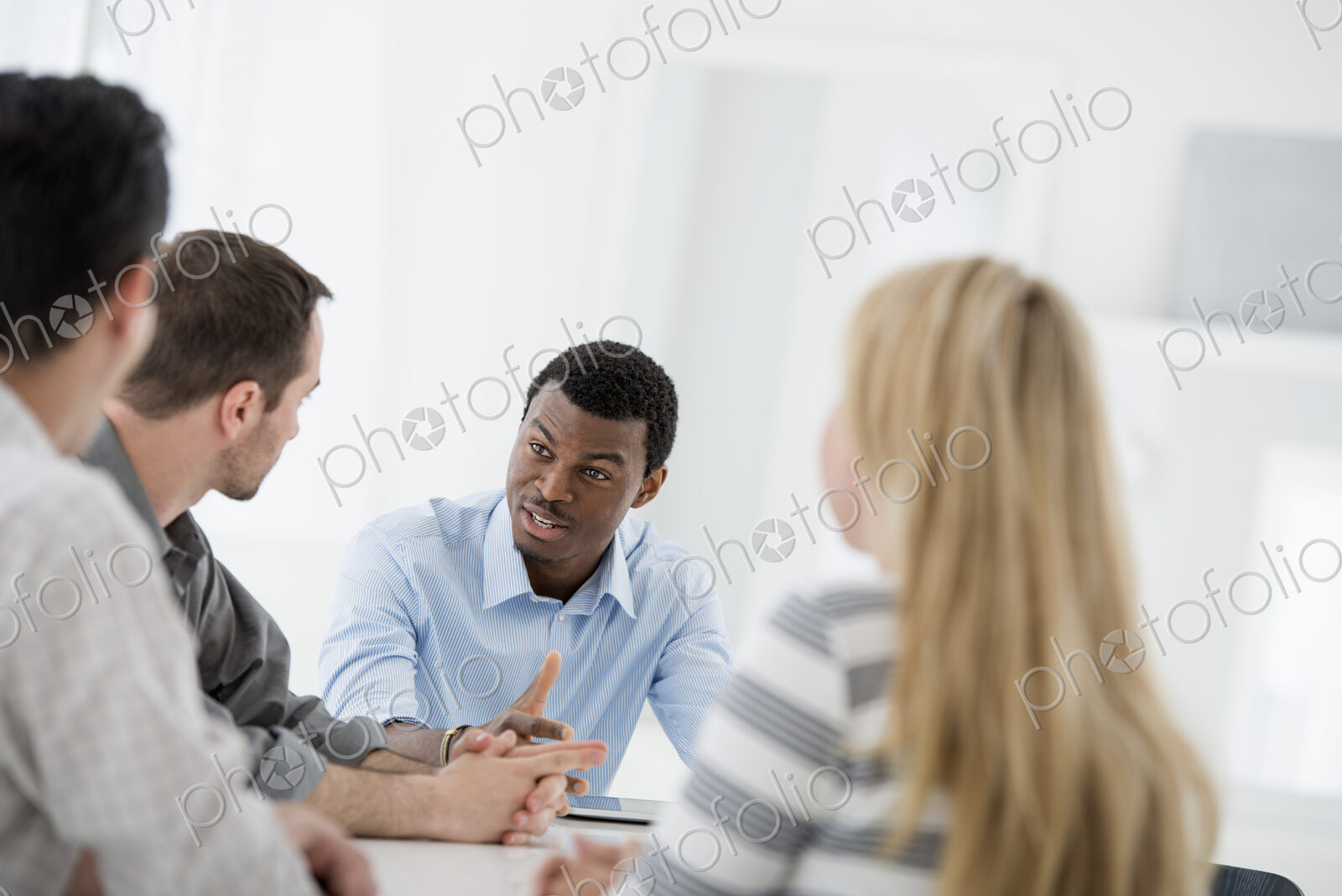 A fresh white building interior, flooded with light. A group of four people, One woman…