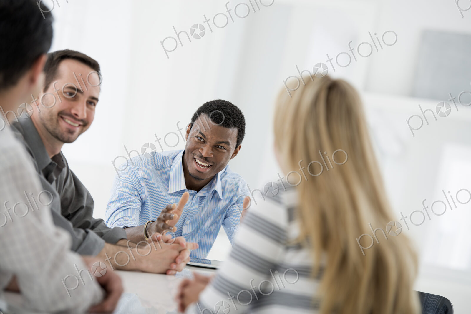 A fresh white building interior, flooded with light. A group of four people, One woman…
