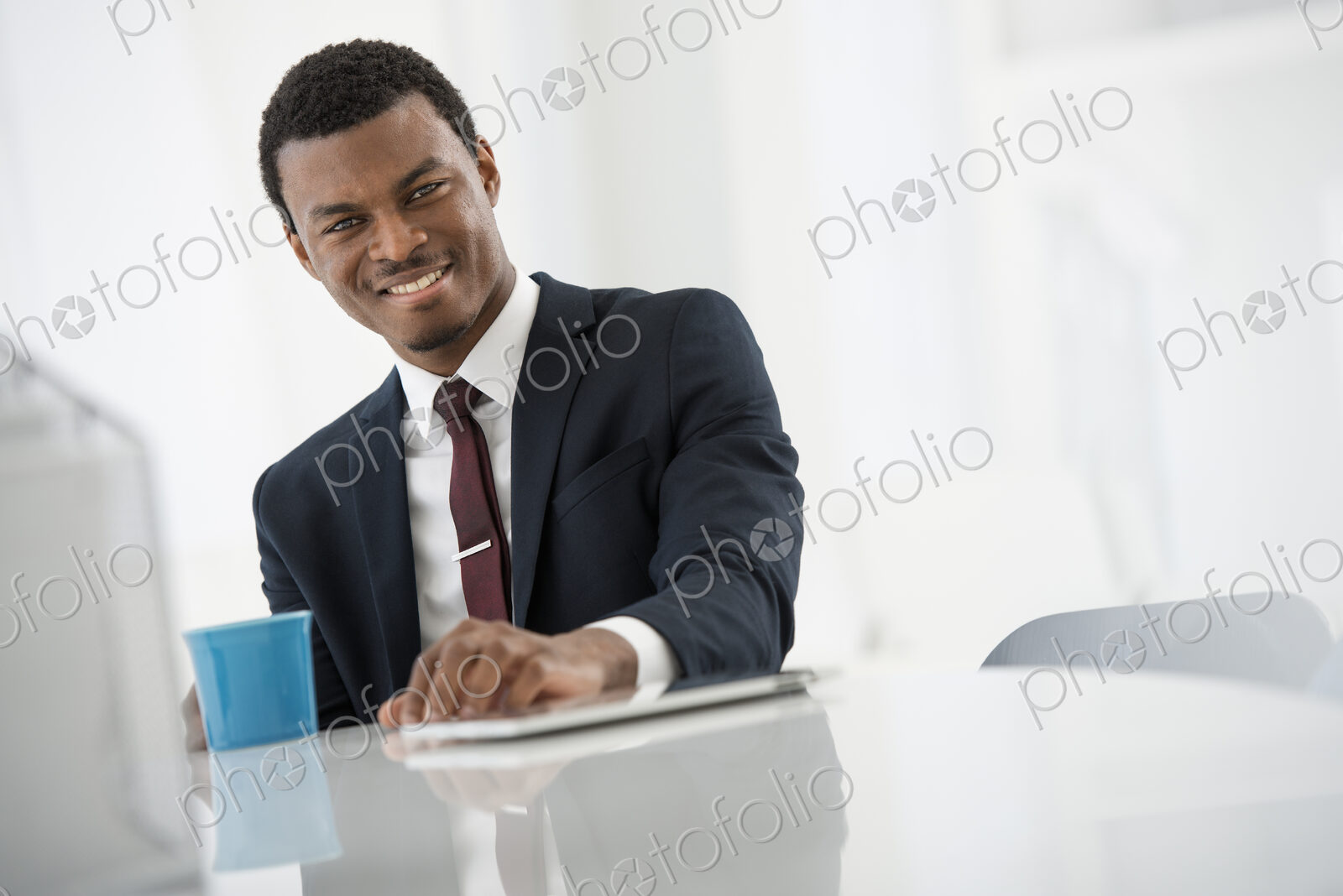 A fresh white building interior, flooded with light. A man in a suit with a cup of…