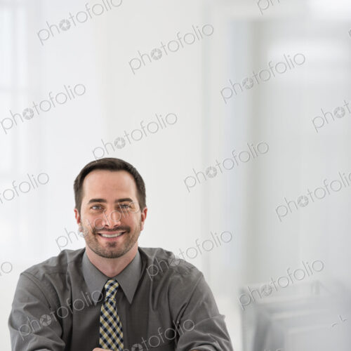 A fresh white building interior, flooded with light. A man seated at a table, beside a… A fresh white building interior, flooded with light. A man seated at a table, beside a…