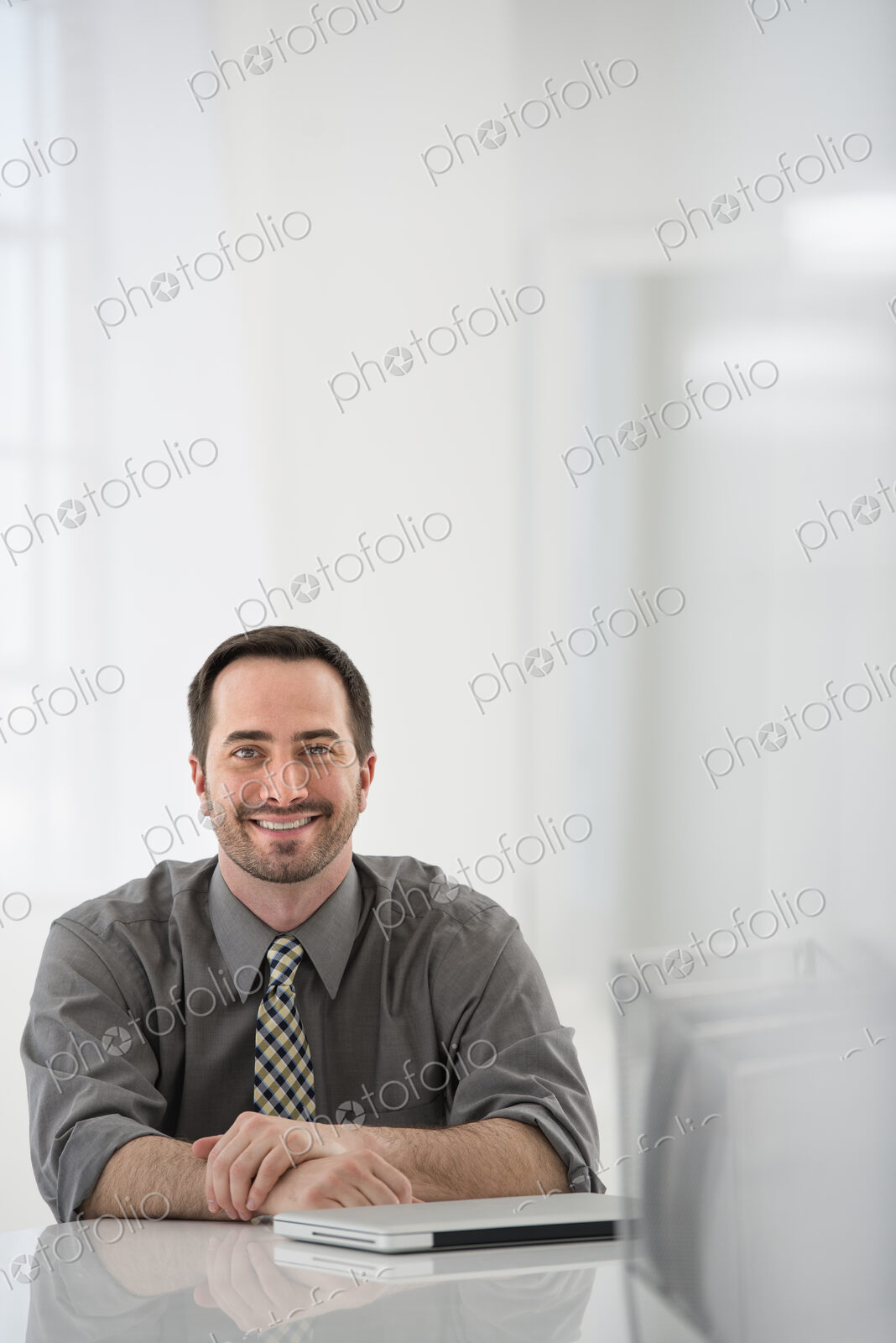A fresh white building interior, flooded with light. A man seated at a table, beside a…