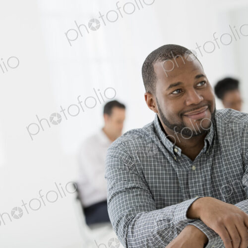 A fresh white building interior, flooded with light. A man seated separately from a… A fresh white building interior, flooded with light. A man seated separately from a…