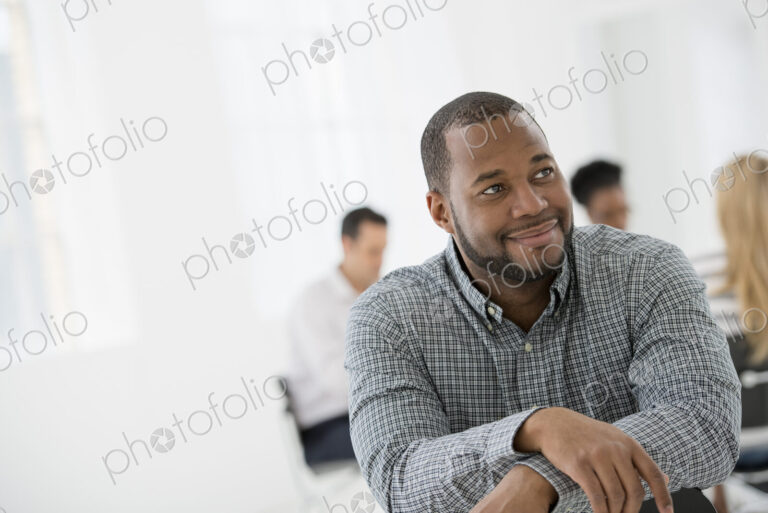 A fresh white building interior, flooded with light. A man seated separately from a…