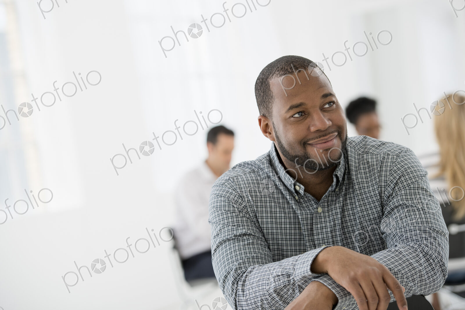 A fresh white building interior, flooded with light. A man seated separately from a…